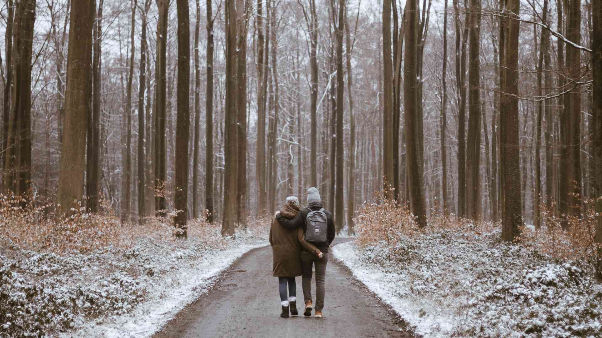 Paar macht einen romantischen Winterspaziergang durch den verschneiten Wald. 